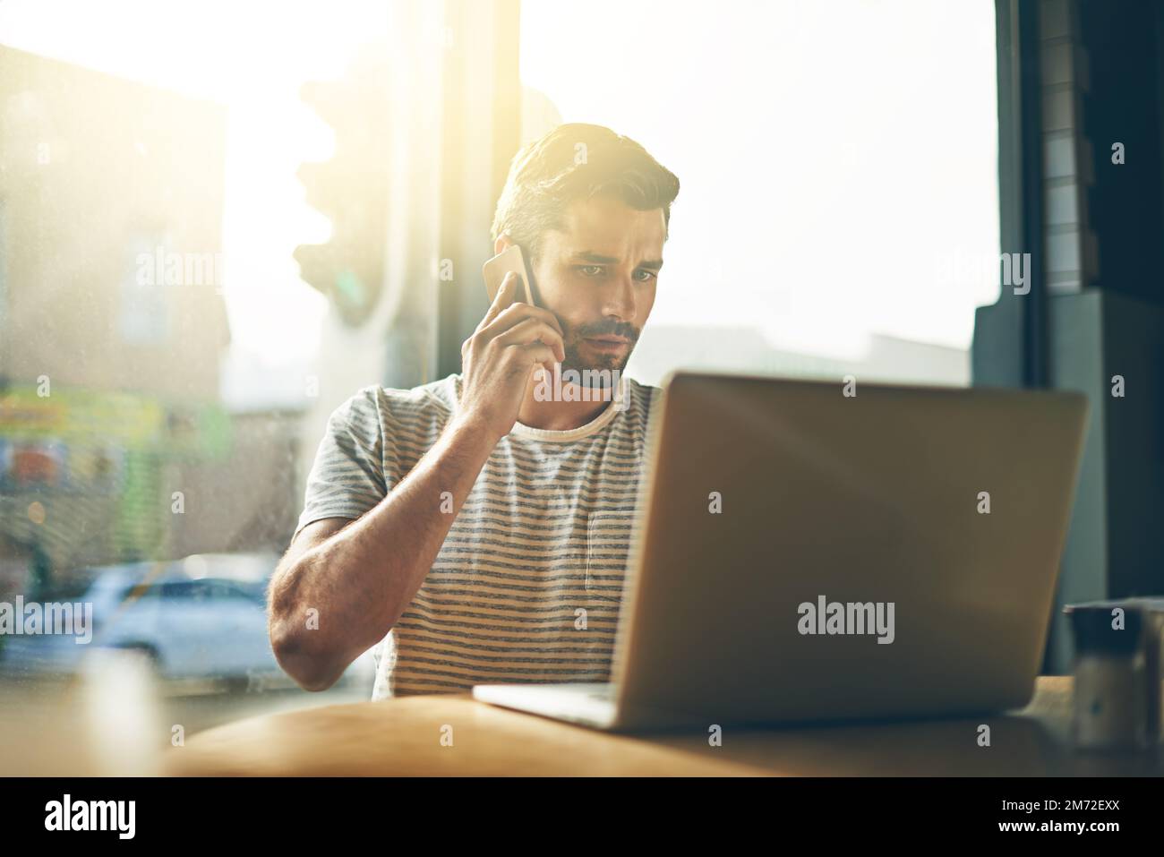 Discuter d'affaires avec un client. Un jeune homme parlant au téléphone tout en étant assis avec son ordinateur portable dans un café. Banque D'Images