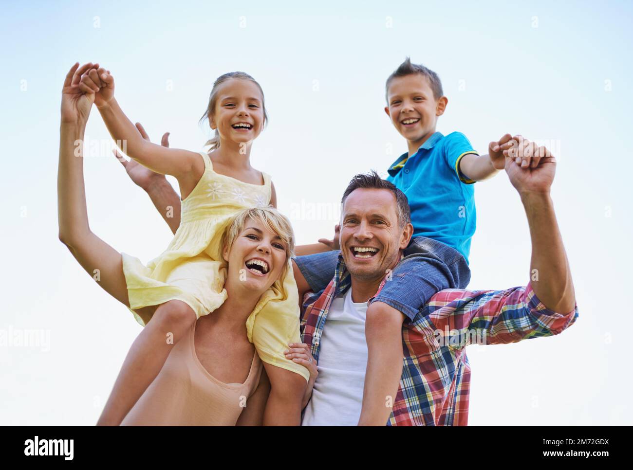 Une famille qui sait comment Amuse-toi bien. Un portrait en bas angle de deux parents heureux portant leurs jeunes enfants sur leurs épaules. Banque D'Images