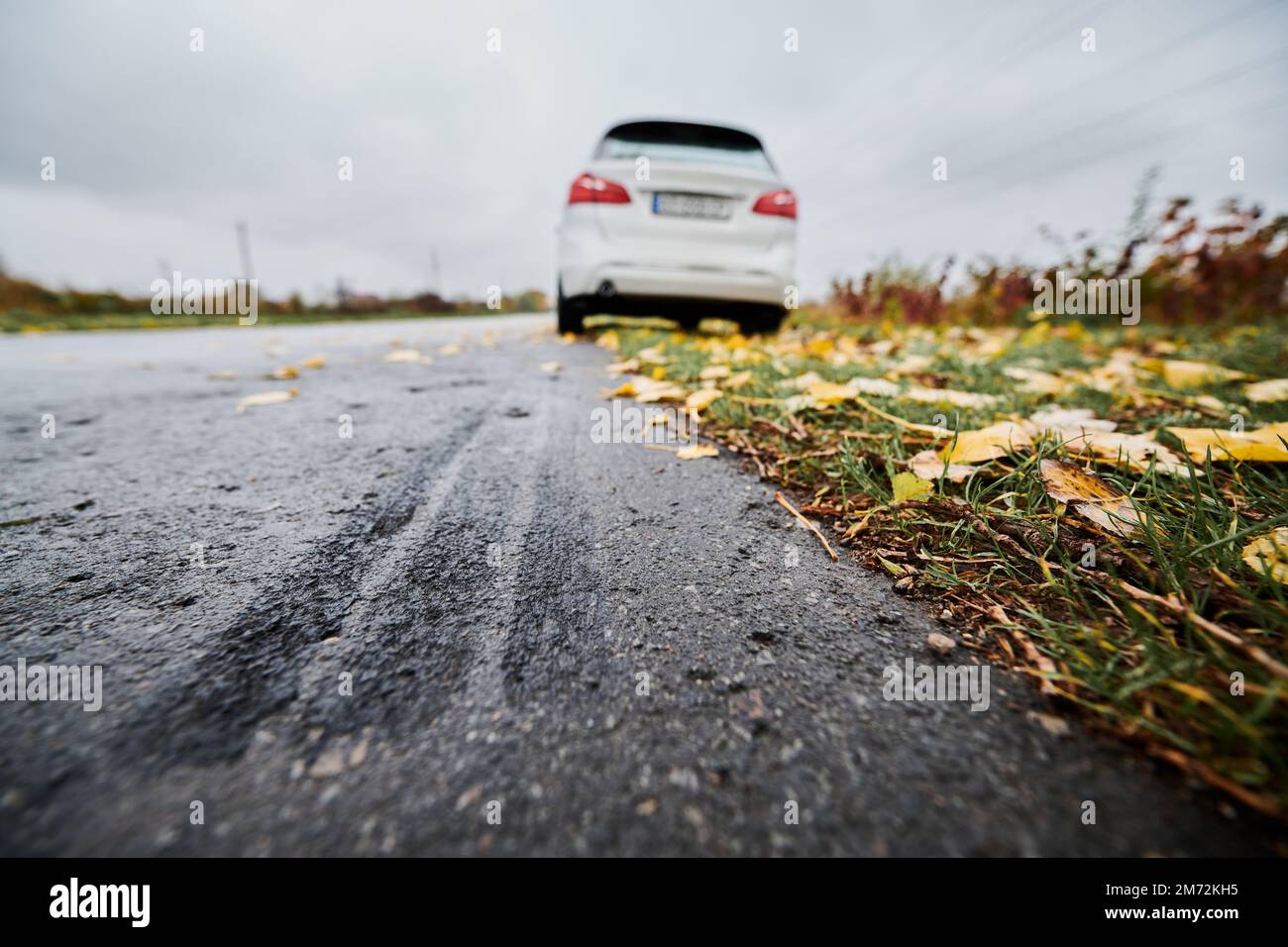Gros plan de la trajectoire du frein de voiture sur le bord de la route asphaltée sur l'arrière-plan de la voiture blanche garée, les feuilles jaunes tombées sur l'herbe et le ciel gris. Voies de freinage d'urgence sur le bord de la route. Banque D'Images