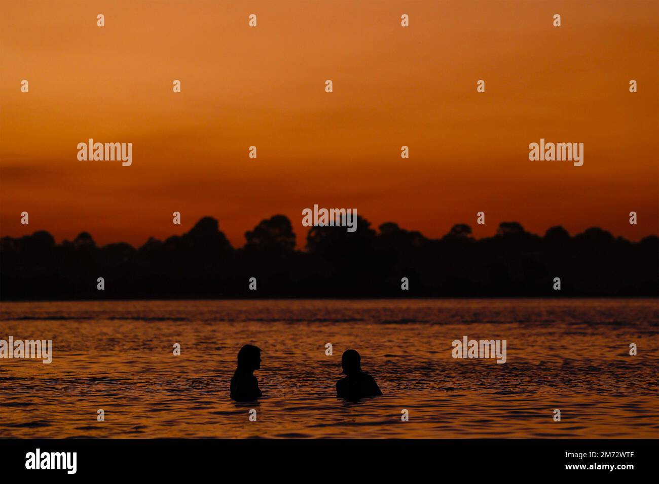 Silhouette de deux personnes dans l'eau contre un ciel de coucher de soleil, Gippsland Lakes, Paynesville, Victoria, Australie. Banque D'Images
