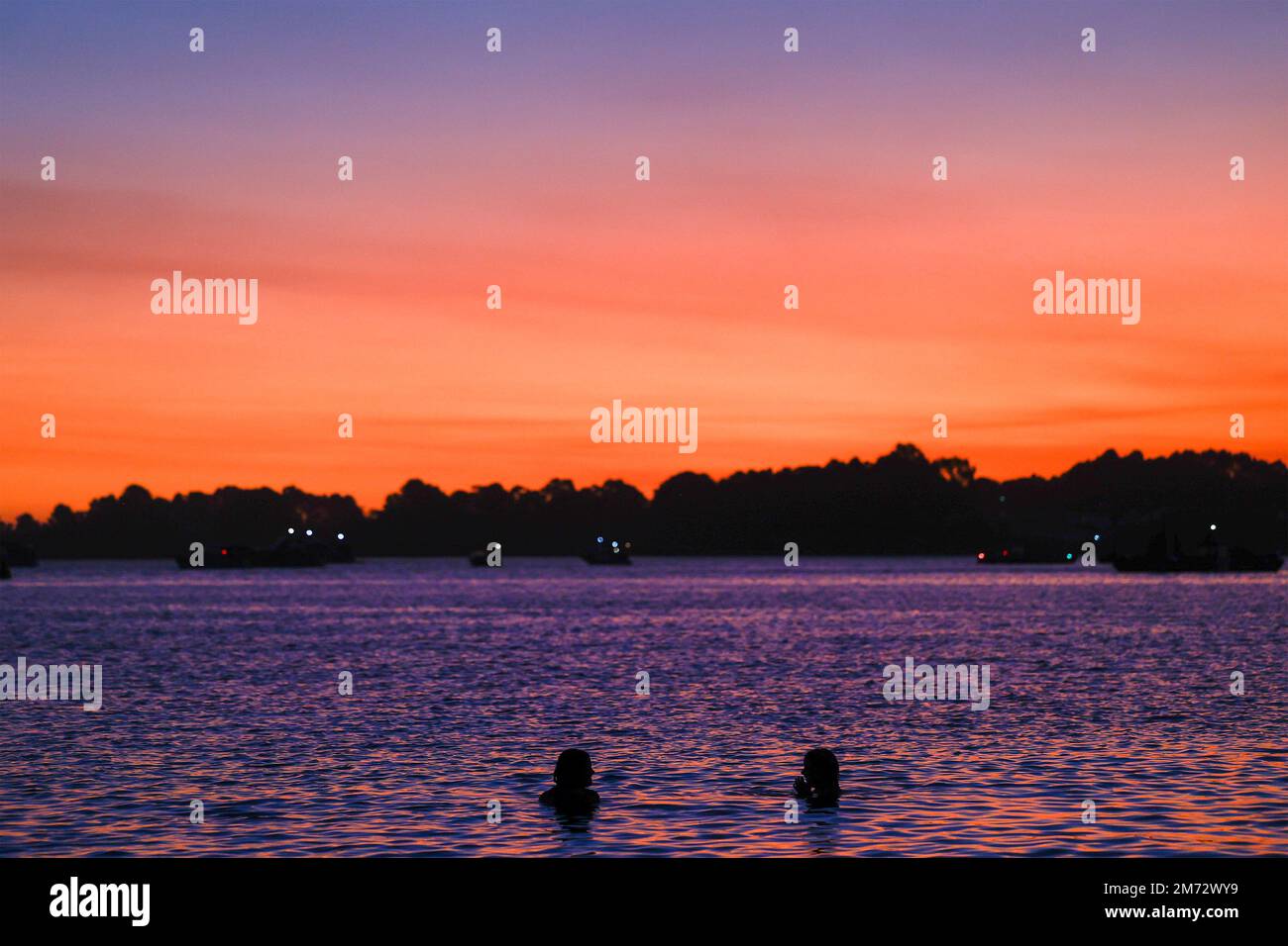 Silhouette de deux personnes dans l'eau contre un ciel de coucher de soleil, Gippsland Lakes, Paynesville, Victoria, Australie. Banque D'Images