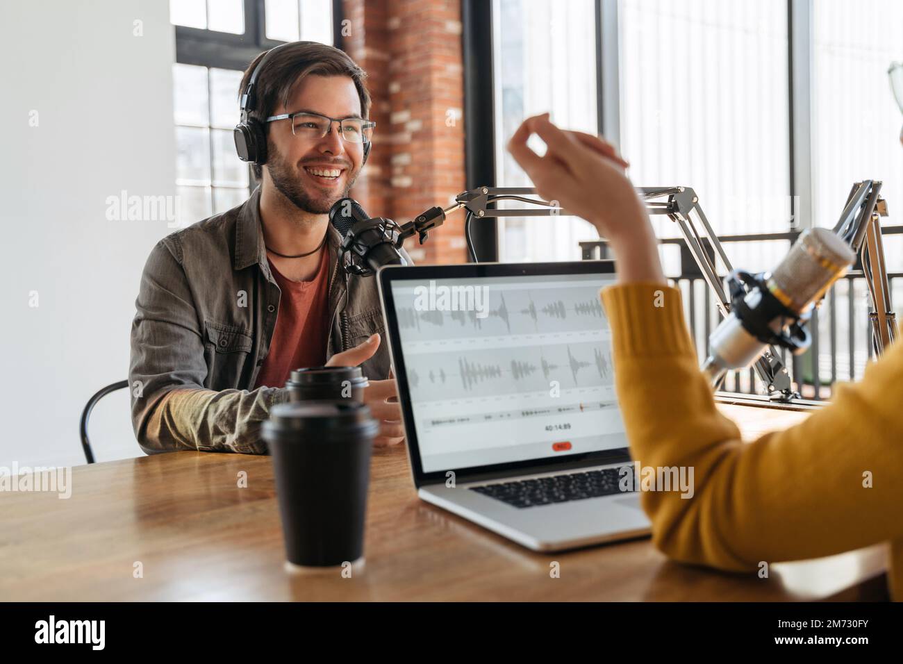 Concept de podcast radio. Invité de radio homme souriant regardant une hôtesse féminine, portant un casque, répondant à une question pour un podcast audio en studio. Femme interrogeant un influenceur célèbre pour le contenu de la chaîne Banque D'Images