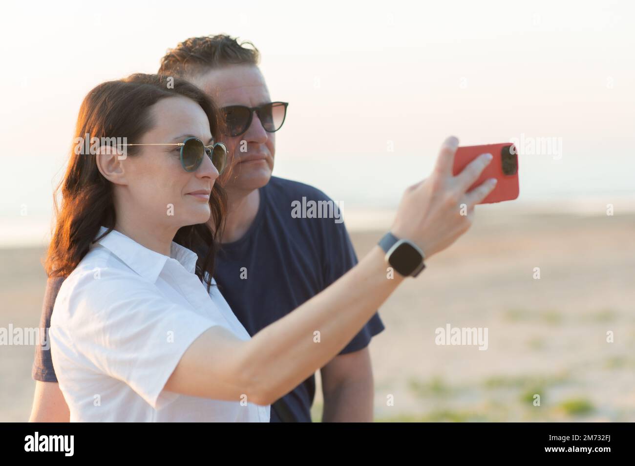 Couple heureux avec différence d'âge - une jeune femme et un homme d'âge moyen prennent un selfie sur la plage Banque D'Images