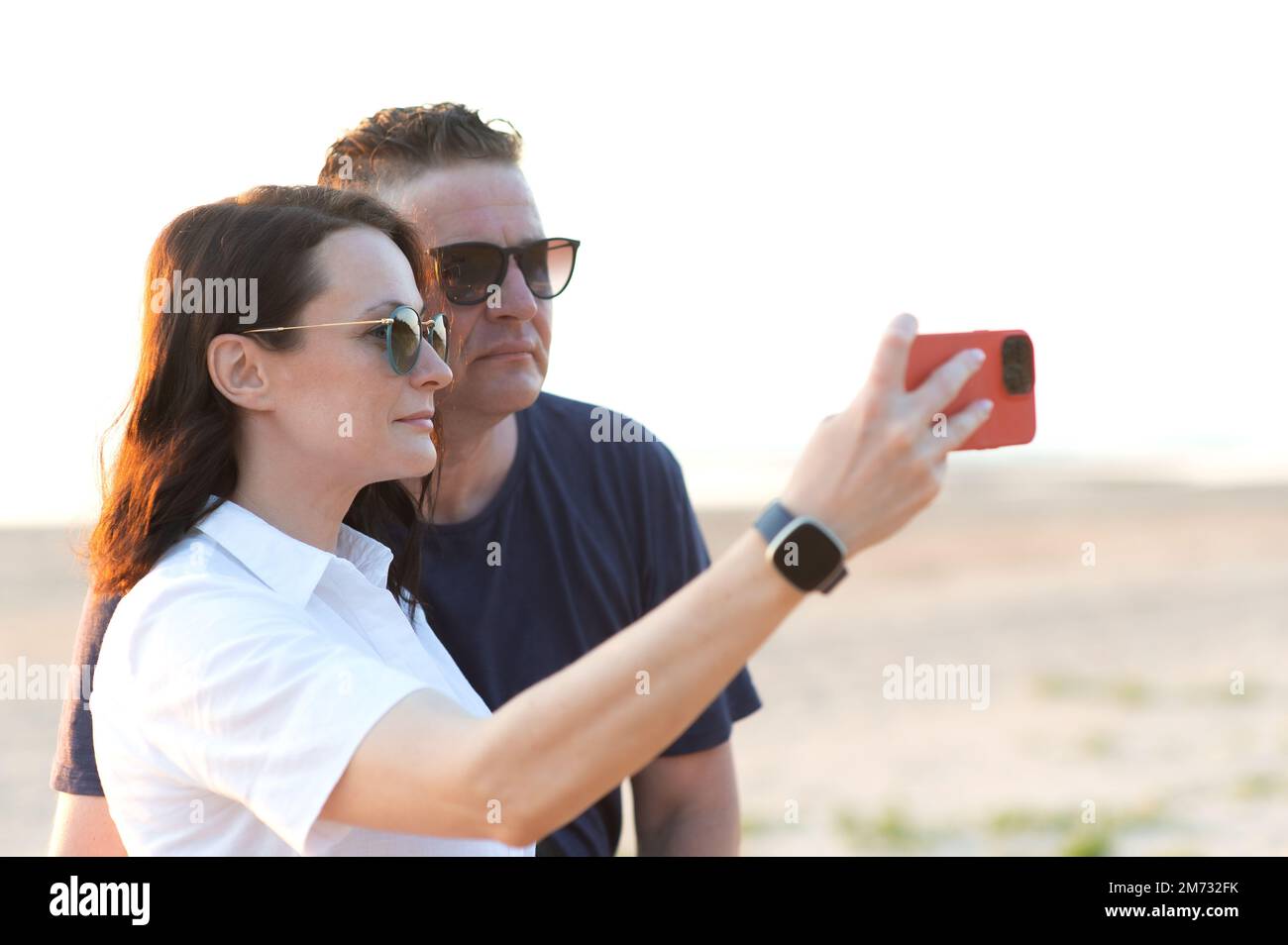 Couple heureux avec différence d'âge - une jeune femme et un homme d'âge moyen prennent un selfie sur la plage Banque D'Images