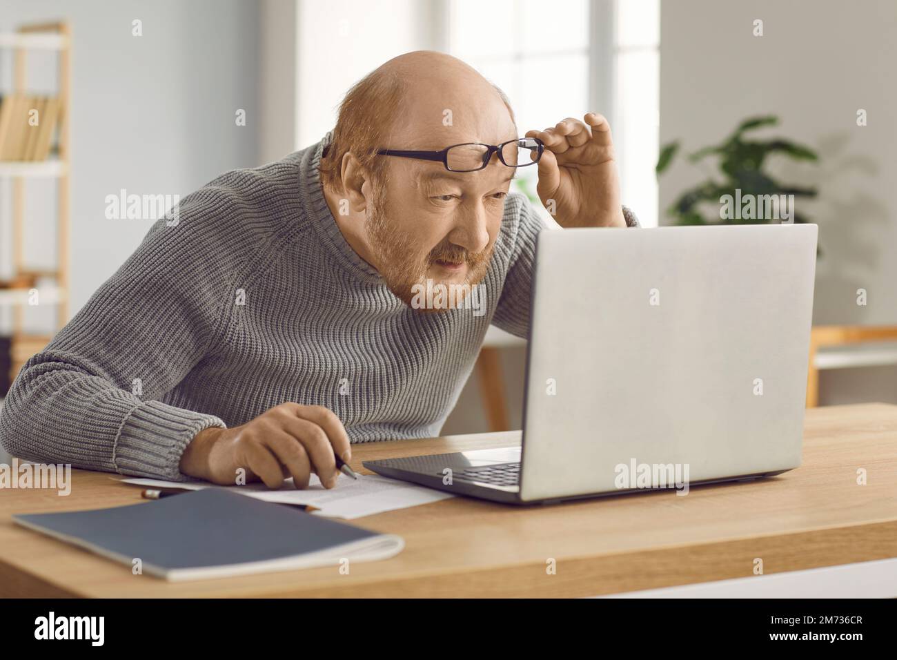 Homme mûr confus qui a une mauvaise vue et travaille sur un ordinateur portable à la maison portant des lunettes. Banque D'Images