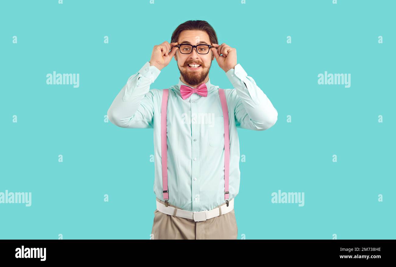 Jeune homme caucasien avec une barbe drôle et une moustache souriante ajuste les lunettes, se tient en studio Banque D'Images