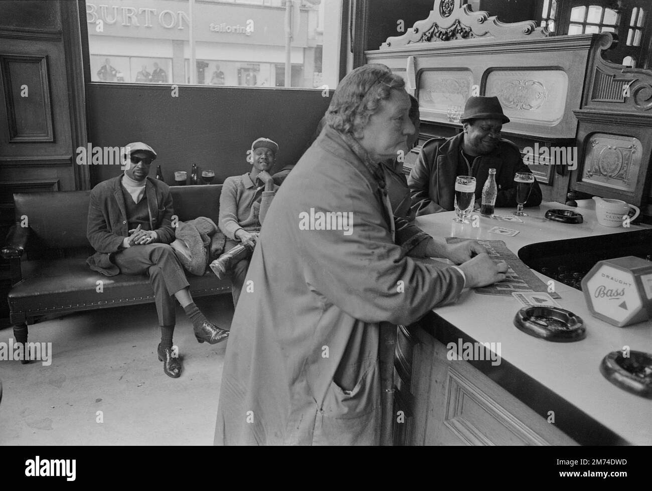 Londres. Fin 1960s. Un groupe d'amis qui se socialisent au pub Duke of Wellington, situé à l'angle de Portobello Road et Elgin Crescent, dans le quartier de Notting Hill du Royal Borough de Kensington et Chelsea, dans l'ouest de Londres. Une dame âgée portant un manteau et un filet à cheveux est debout au bar, attendant d'être servie. Banque D'Images