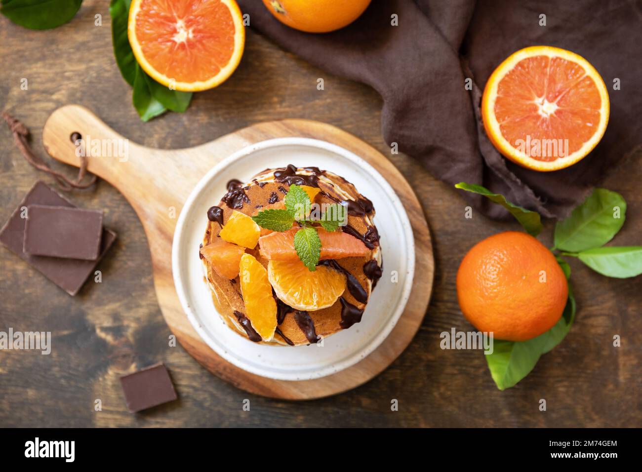 Fêtez la fête du Pancake, petit déjeuner américain sain. Délicieuses crêpes aux bananes avec chocolat et oranges rouges sur table rustique. Vue de dessus. Banque D'Images