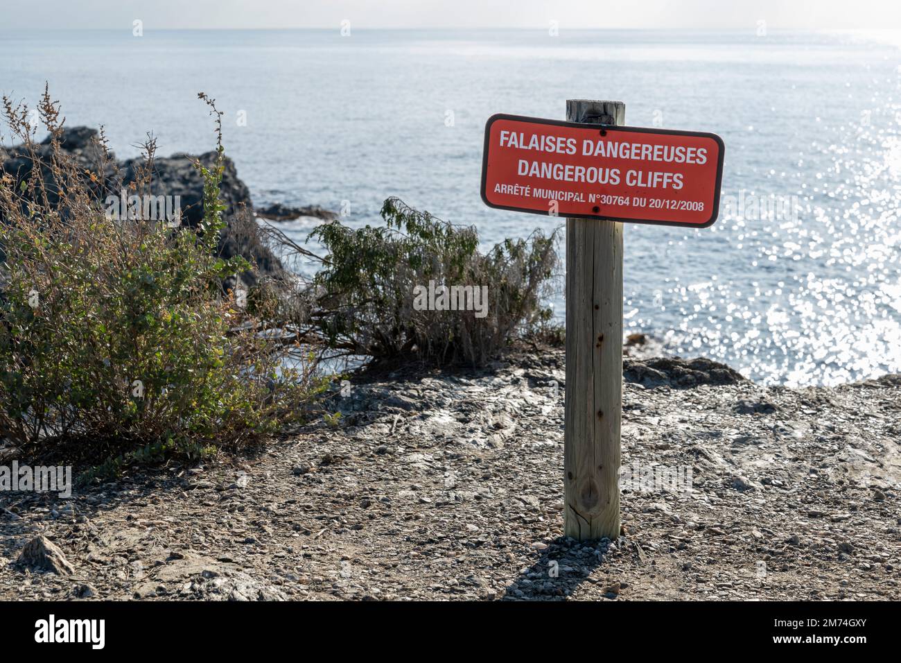 Panneau d'avertissement et d'information rouge dans le sud de la France devant les falaises et lettres bilingues français anglais indiquant les falaises dangereuses Banque D'Images