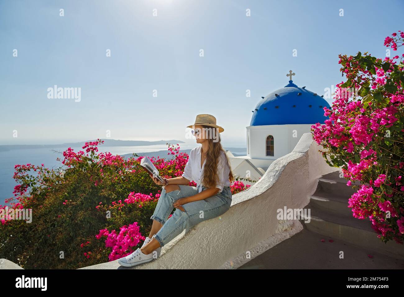 Une jeune femme lit un livre assis sur le remblai de l'île de Santorini, en Grèce. Banque D'Images