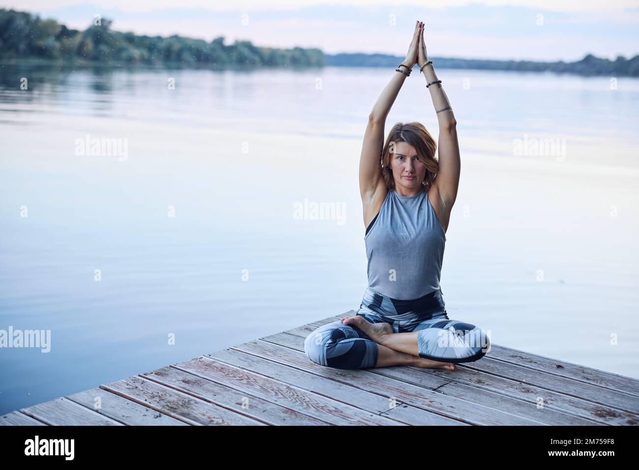 Une femme calme dans la posture du lotus s'assoit sur un quai et pratique la respiration de yoga près de la rivière. Banque D'Images