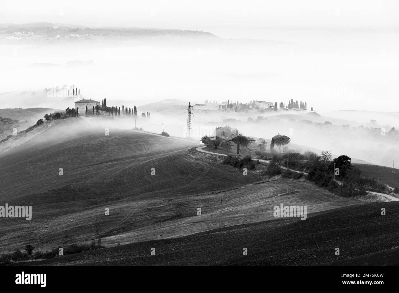 Maisons de campagne sur le paysage vallonné dans la brume matinale, noir et blanc tourné, près de Sienne, Toscane, Italie Banque D'Images