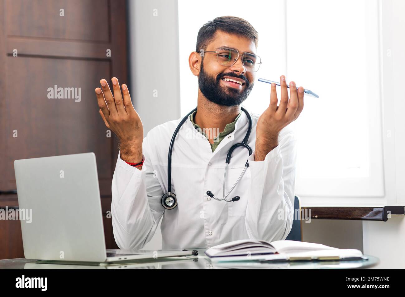 Médecin indien joyeux enregistrant un message vocal sur un téléphone portable à l'hôpital Banque D'Images