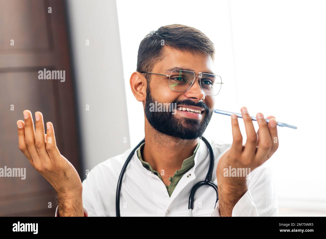 Médecin indien joyeux enregistrant un message vocal sur un téléphone portable à l'hôpital Banque D'Images