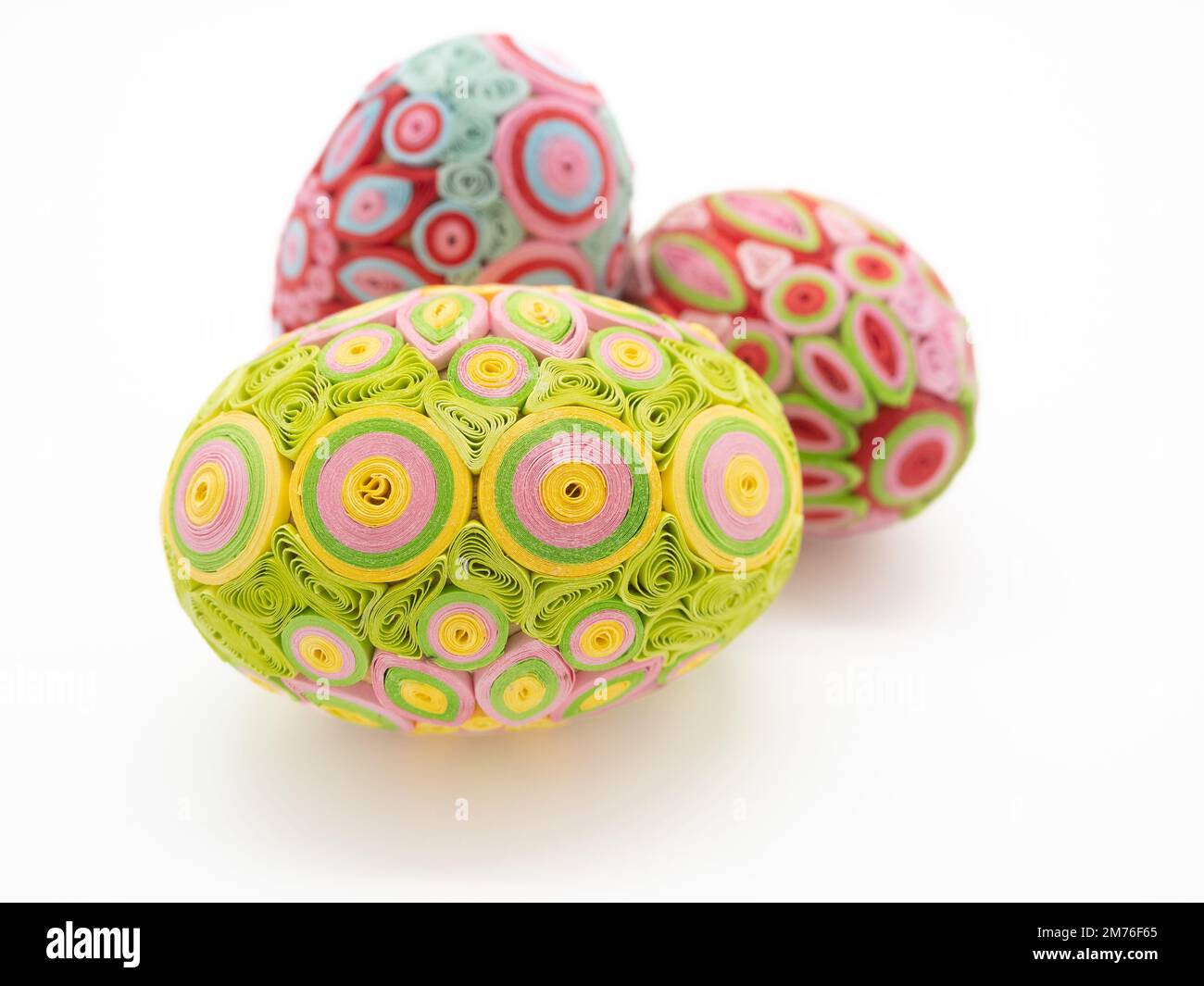 Gros plan de trois œufs de Pâques sur fond blanc. Les œufs sont vert lime, rose, jaune et fuchsia. Banque D'Images