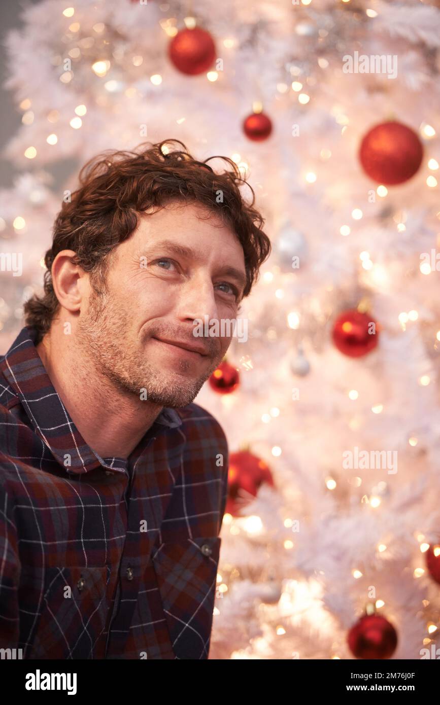 Rêver d'un Noël blanc. Un bel homme devant un arbre de Noël blanc. Banque D'Images