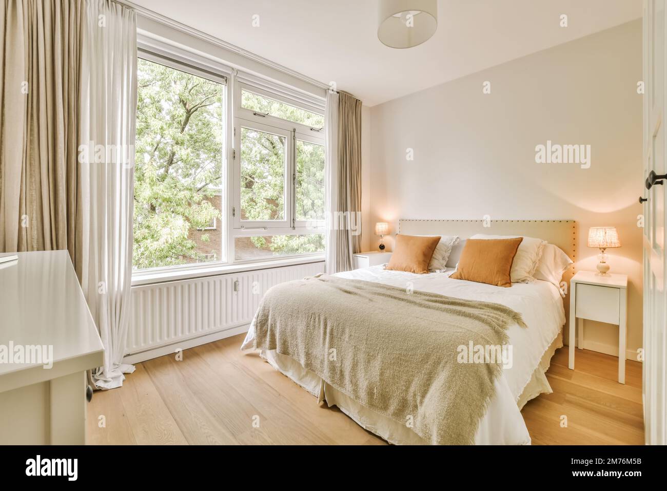 une chambre avec murs blancs et parquet la chambre a une grande fenêtre qui donne sur les arbres à l'extérieur Banque D'Images