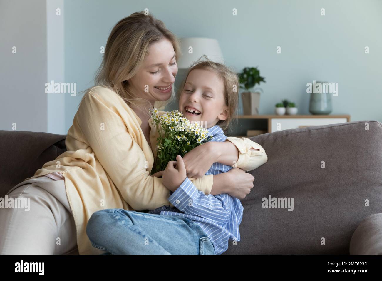 Bonne maman embrassant mignonne petite fille gaie enfant tenant des fleurs Banque D'Images