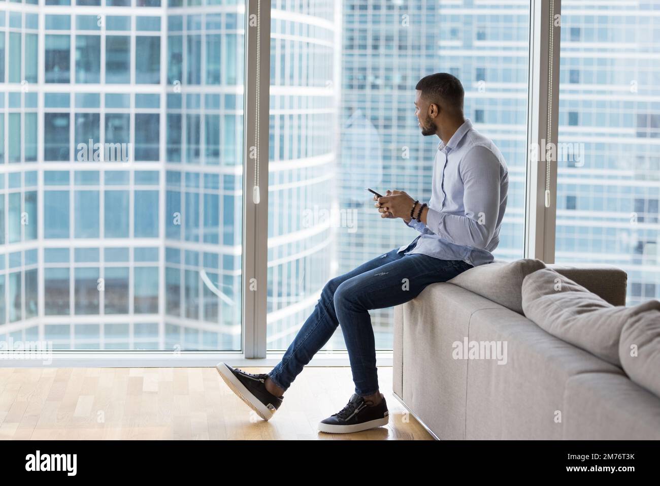 Un homme d'affaires africain tient un smartphone qui regarde les grands bâtiments urbains Banque D'Images