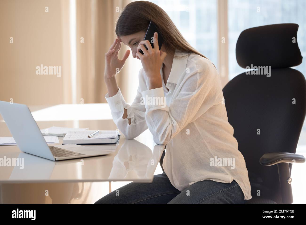 Femme d'affaires assise à un bureau ayant une conversation désagréable sur un téléphone portable Banque D'Images