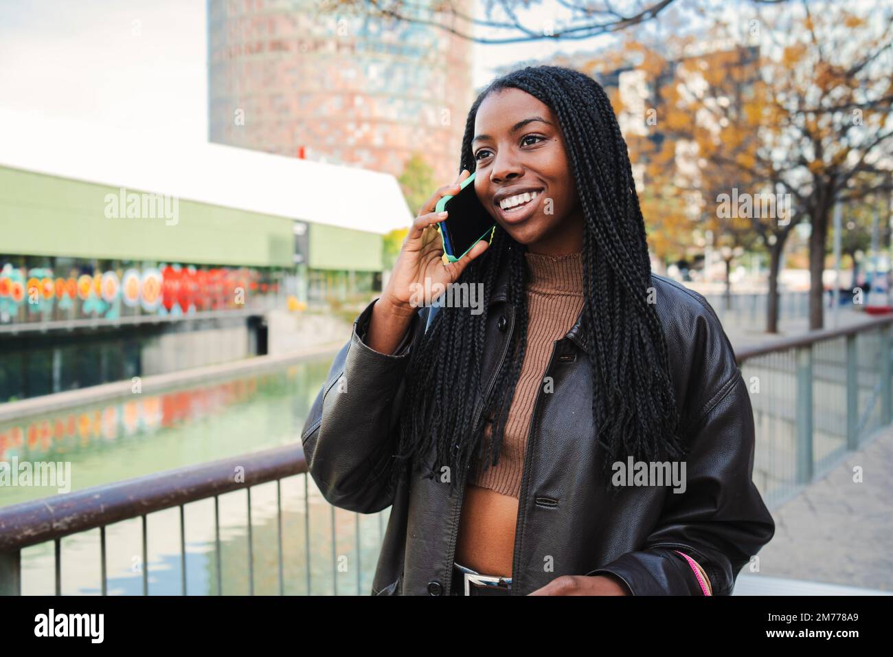 Bonne femme afro-américaine souriante et parlant au téléphone portable à l'extérieur. Jeune femme discutant sur une conversation téléphonique par téléphone intelligent. Concept de communication. Photo de haute qualité Banque D'Images