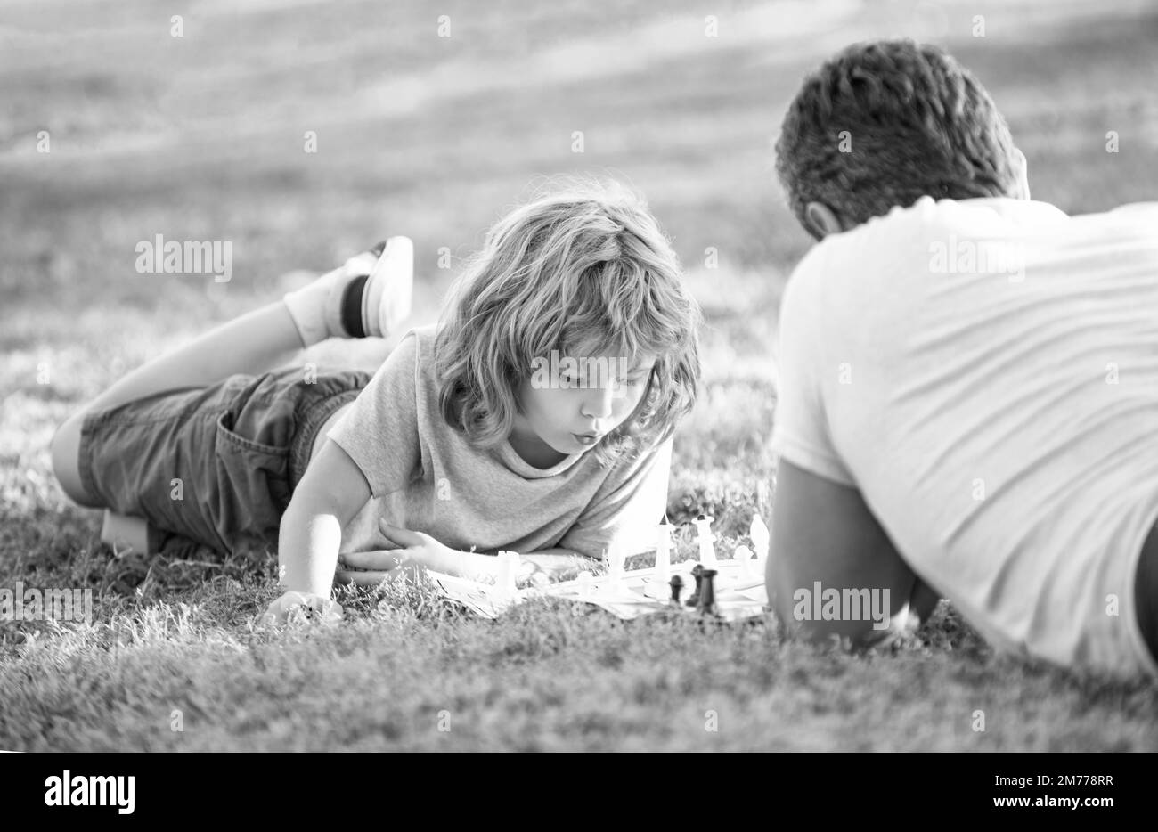 bonne famille de papa et garçon de fils jouant aux échecs sur l'herbe verte dans le parc extérieur, stratégique Banque D'Images