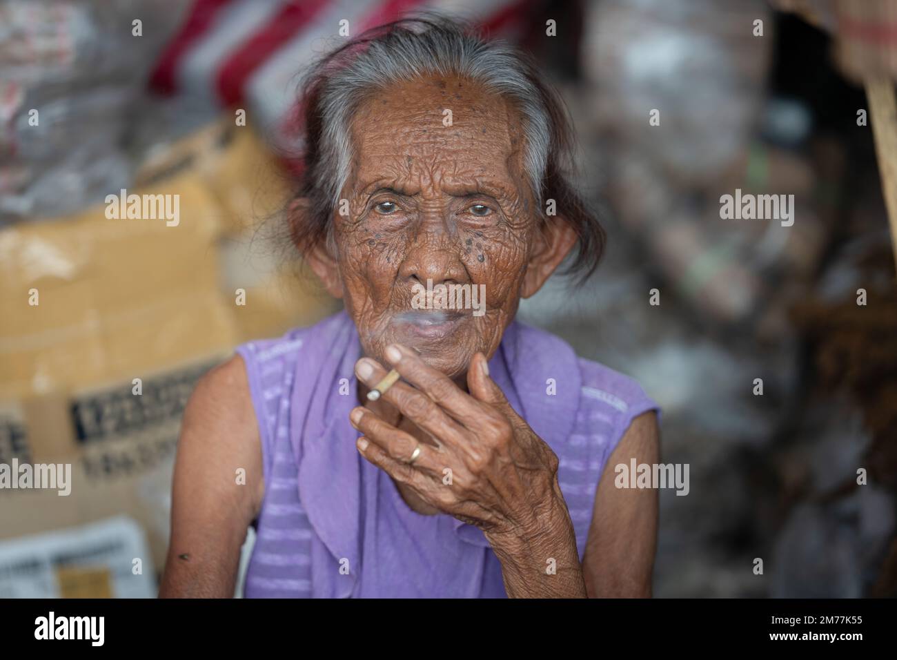 Portrait d'une femme âgée fumant une cigarette tout en vendant des feuilles de tabac sur un marché de rue, Cebu City, Philippines Banque D'Images