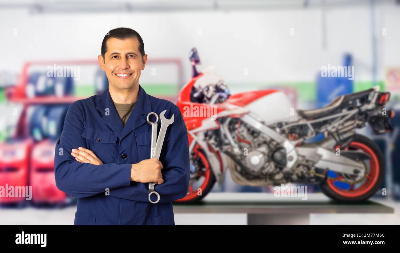 Vue de face d'un mécanicien de moto se posant debout en vous regardant dans un atelier mécanique et un espace de copie Banque D'Images