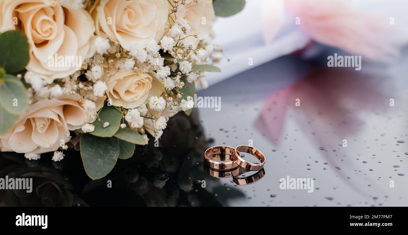 Une belle image aux tons avec des anneaux de mariage se trouve sur une surface noire sur le fond d'un bouquet de fleurs Banque D'Images Une belle image aux tons avec des anneaux de mariage se trouve sur une surface noire sur le fond d'un bouquet de fleurs Banque D'Images