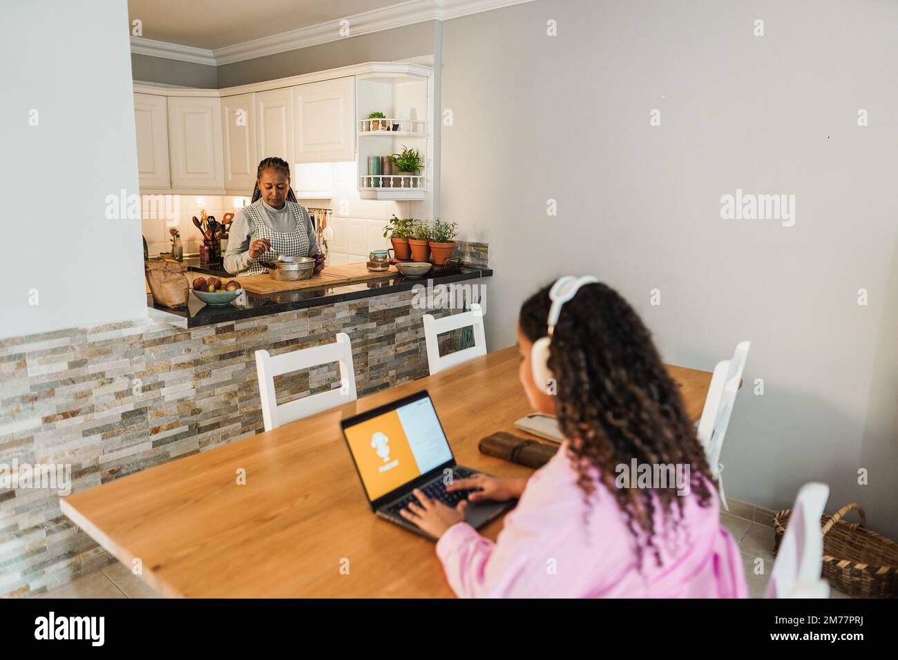 Fille africaine utilisant un ordinateur portable tandis que la mère cuisine à la maison - attention douce sur le visage de femme senior Banque D'Images