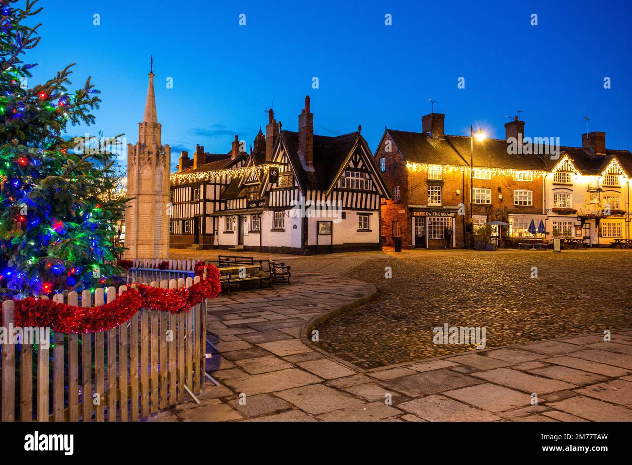 La place du marché pavée de Sandbach à Cheshire avec son arbre de Noël et ses lumières et le mémorial de guerre du cénotaphe et l'auberge de coaching noir et blanc Banque D'Images