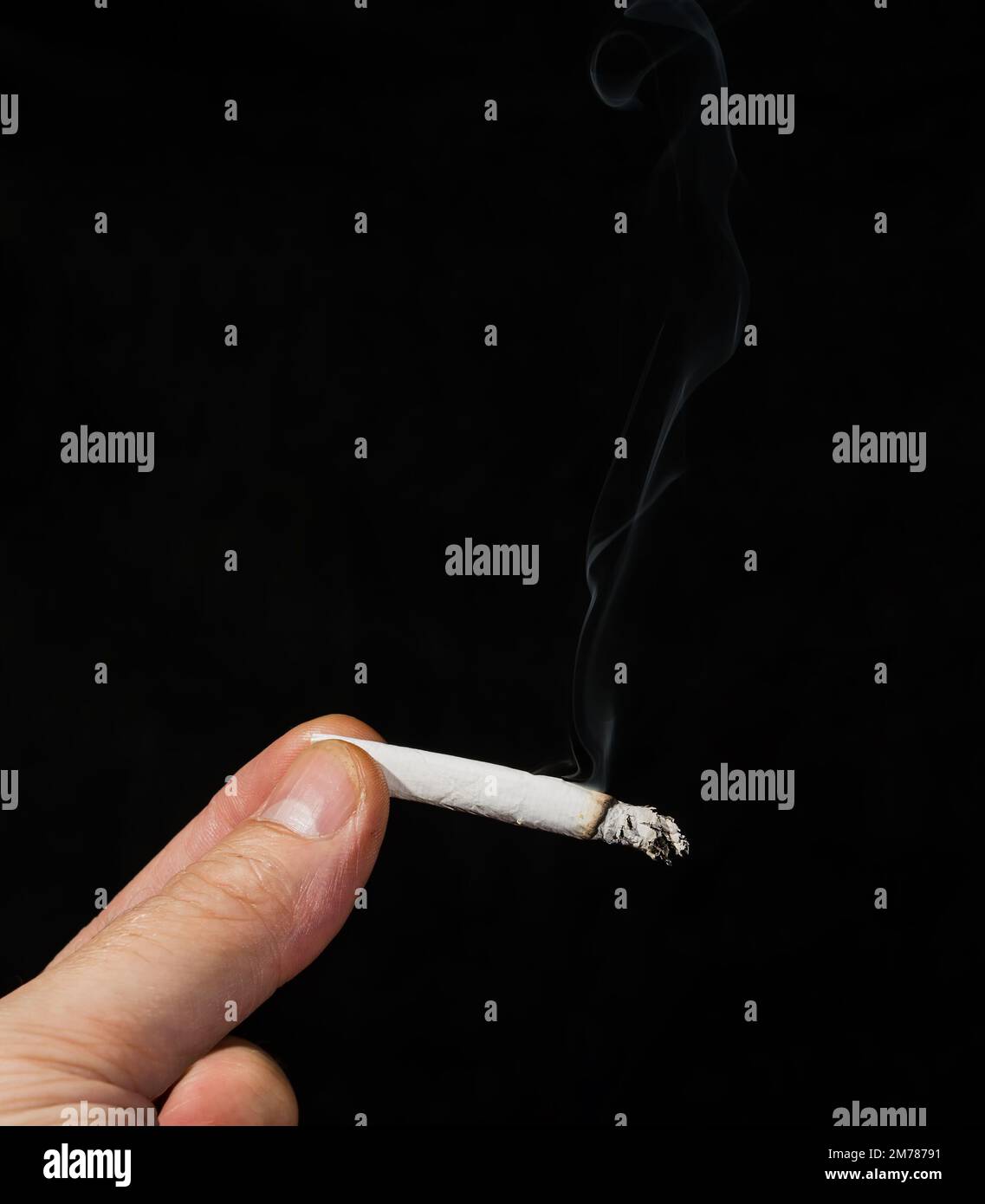 Une main tenant une cigarette de marijuana allumée. De la fumée s'échappe du joint et le fond est légèrement voilé en raison de la fumée dans la chambre. Banque D'Images