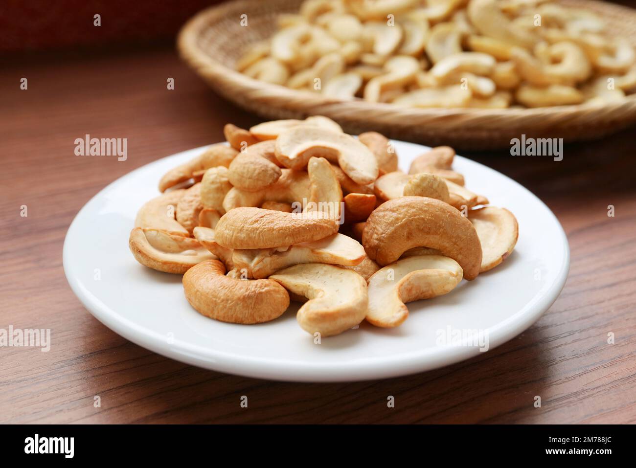 Une assiette de délicieux noix de cajou rôties avec les noix de cajou non cuites en toile de fond Banque D'Images