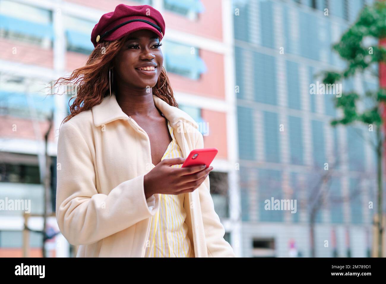 Femme souriante tenant un téléphone portable tout en marchant dans la rue. Banque D'Images