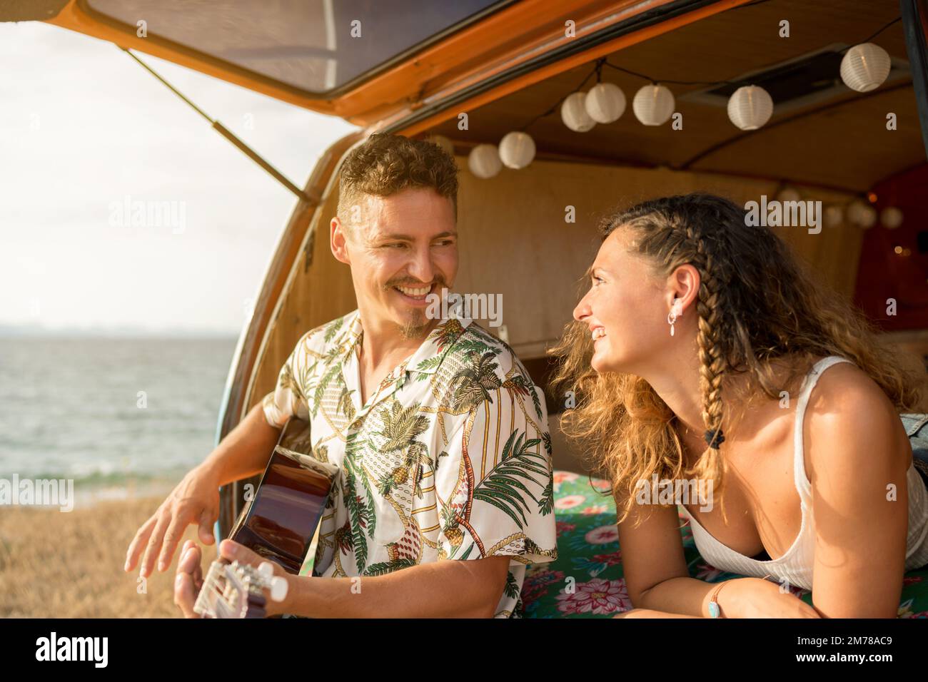 Scène romantique d'un heureux homme jouant la guitare à côté d'une femme à l'intérieur d'une camionnette de camping Banque D'Images