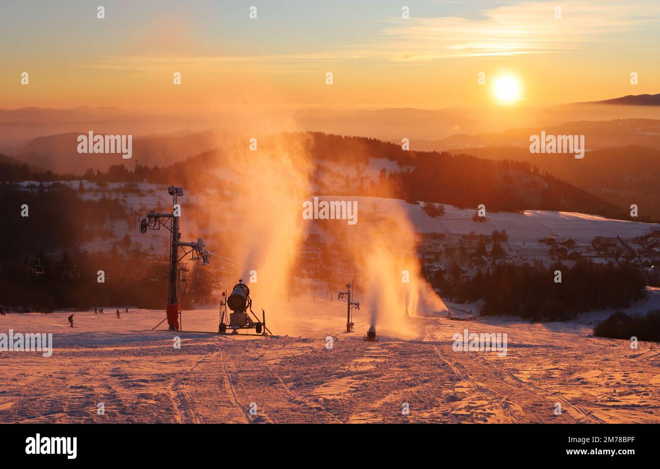 Piste de ski dans la station d'hiver avec des skieurs et des canons à neige au coucher du soleil, Slovaquie Banque D'Images