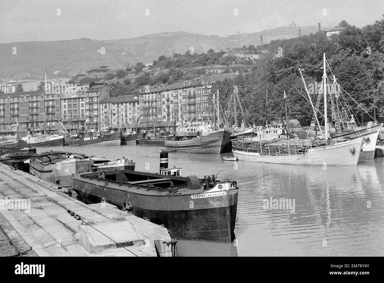 Remorqueurs et bateaux de cargaison ou navires en bois avec grumes de bois dans le port ou le port avec le quai et le front de mer Bergen Norvège c1960. Photographie noir et blanc ou monochrome vintage. Banque D'Images