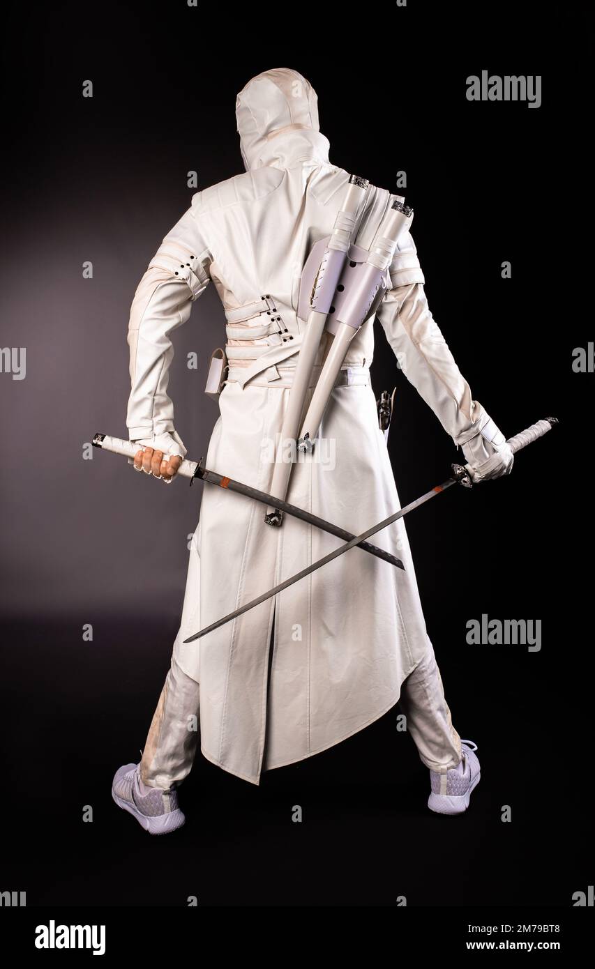 Homme debout avec son dos sous la forme d'un ninja de combat posant avec deux épées sur un fond noir. Banque D'Images