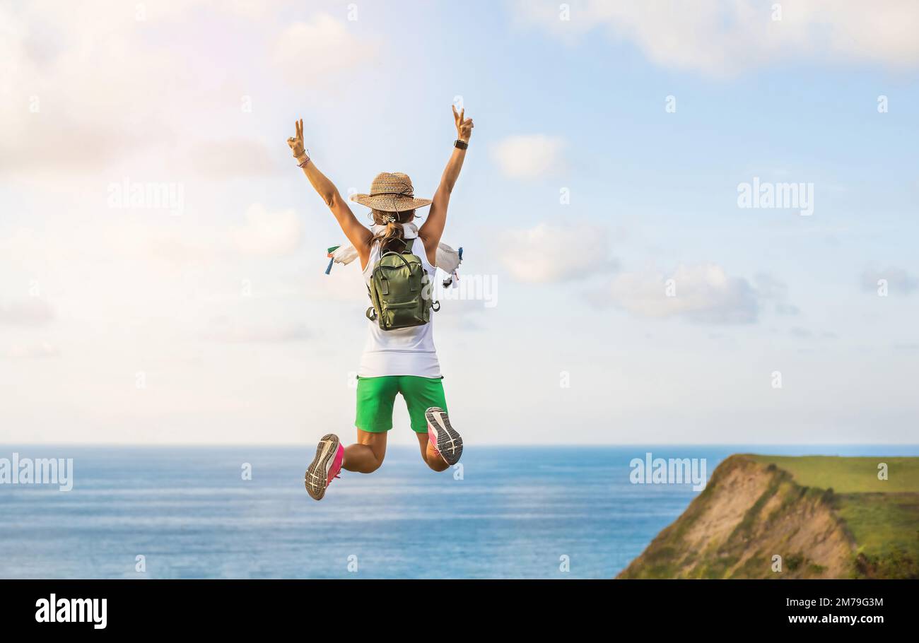 une femme avec son dos tourné, saute avec ses bras vers le haut et ses jambes repliées. Concept du bonheur, de la liberté et de la nature. Banque D'Images