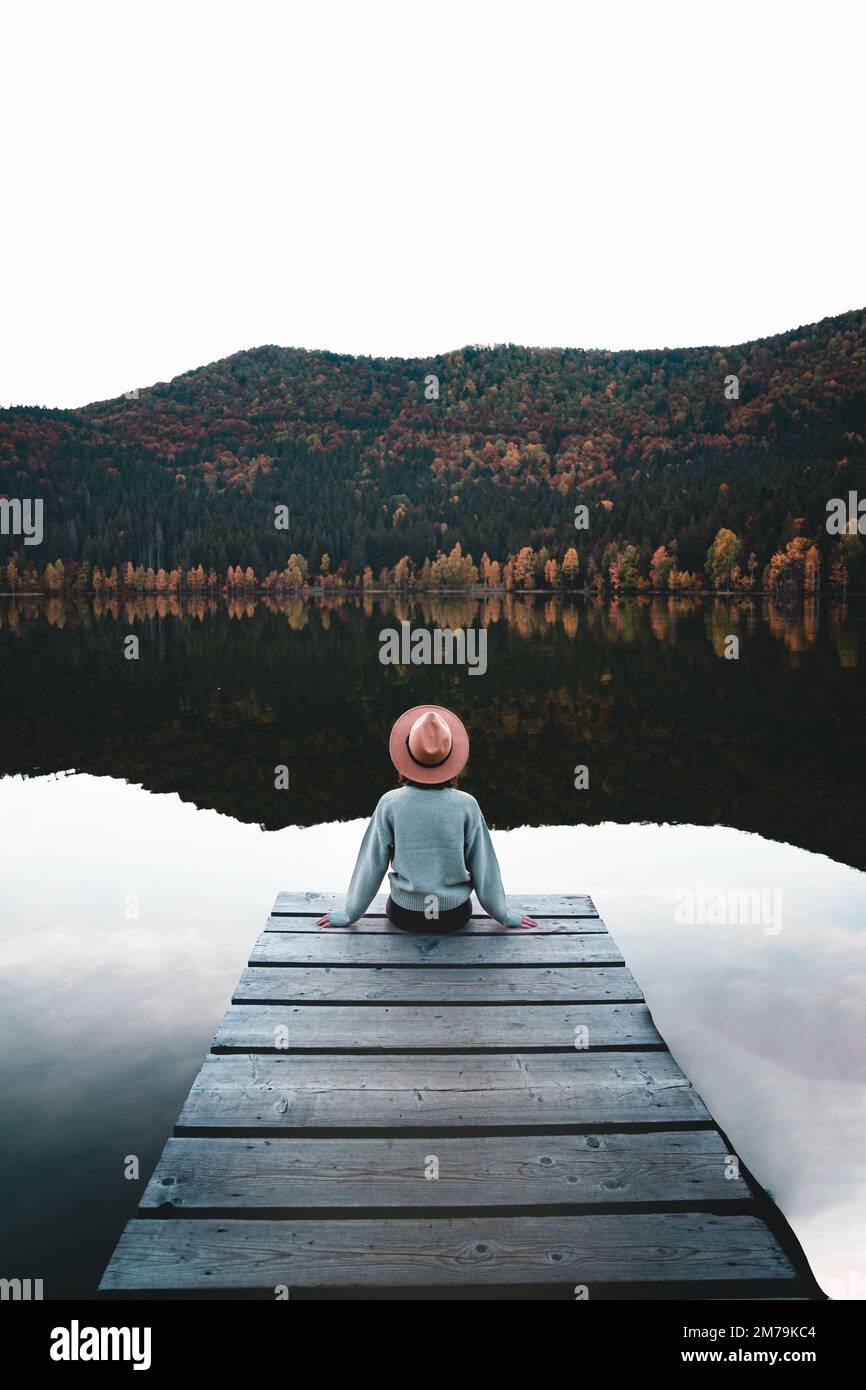 Vue arrière d'une jeune femme à l'ancienne assise sur un quai en bois donnant sur la vue sur le lac Banque D'Images