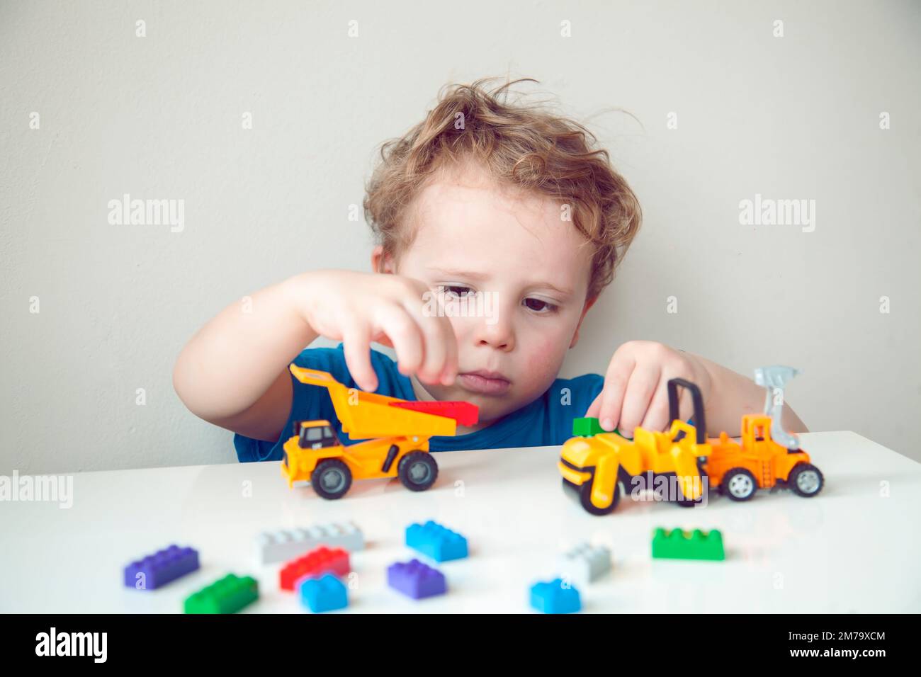 Garçon joue des cubes multicolores et des voitures sur la table. Développement et apprentissage précoces. Banque D'Images