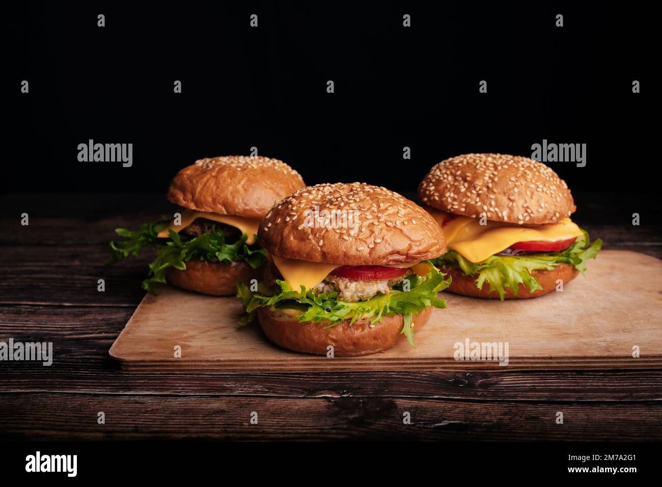 Trois hamburgers juteux avec de la viande, du fromage, de la laitue, de la tomate sur une planche en bois sur la table Banque D'Images