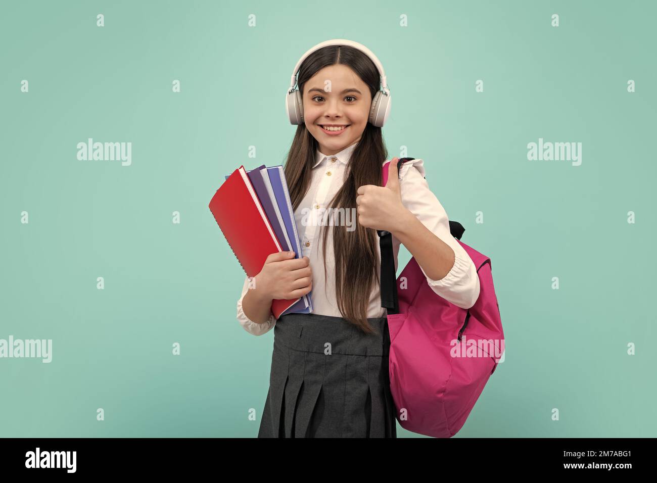 Fille d'école, étudiante adolescente dans des écouteurs et des livres sur fond isolé de studio. Enfants avec sac à dos. Banque D'Images