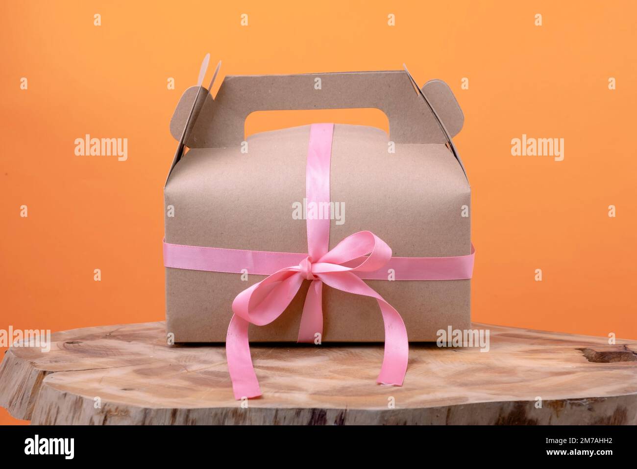 Préparer une boîte cadeau avec un petit ruban rose sur bois sur fond orange. Concept de décoration écologique du nouvel an et de Noël Banque D'Images
