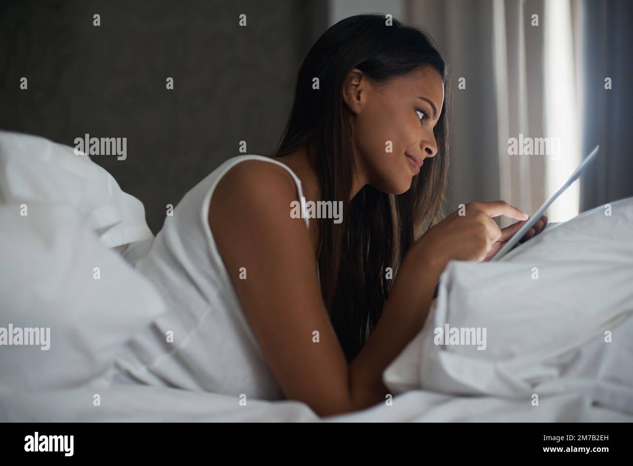 Des histoires modernes au coucher du lit. une belle jeune femme se reposant au lit avec sa tablette. Banque D'Images