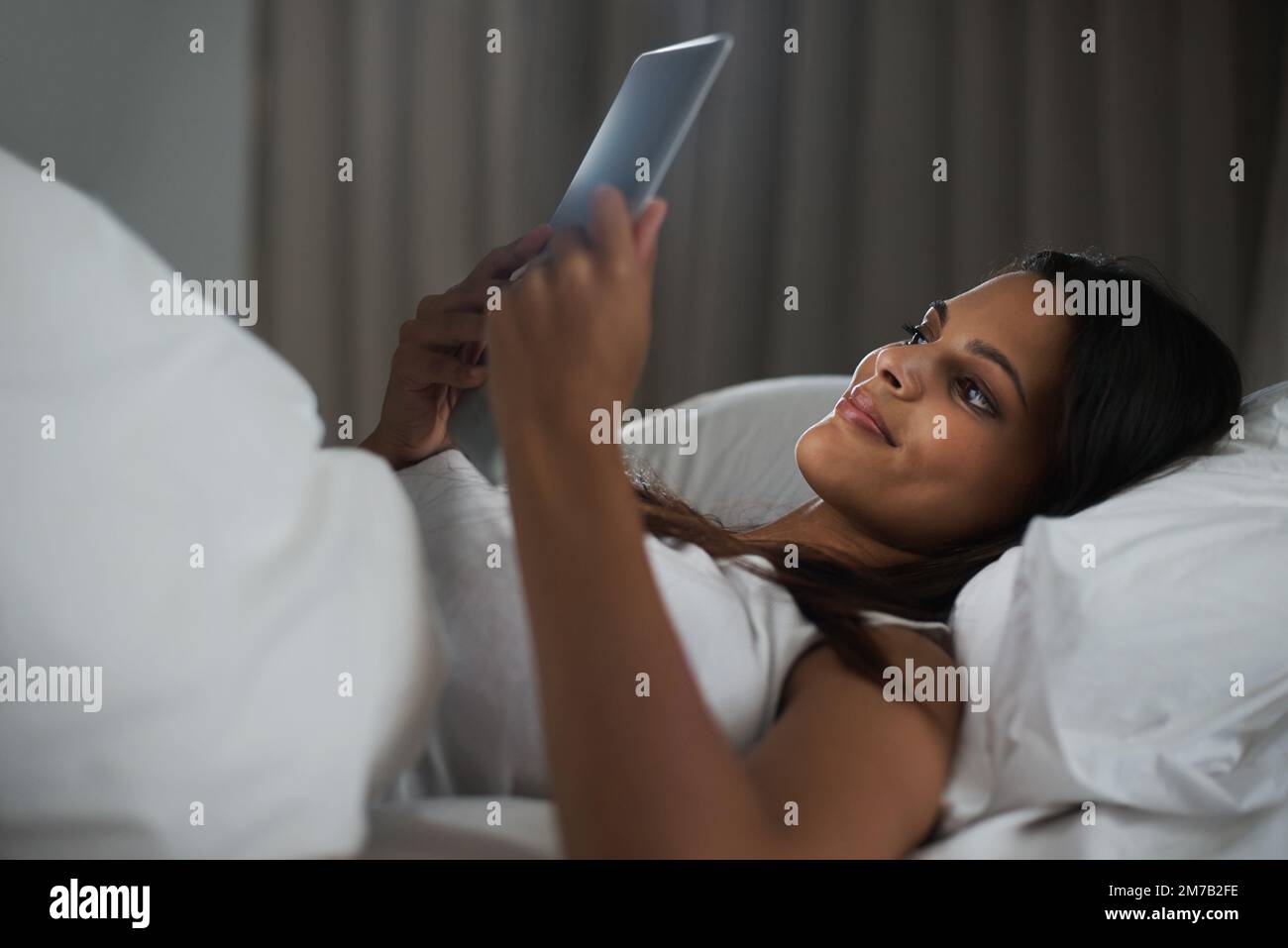 En ligne la nuit. une belle jeune femme se reposant au lit avec sa tablette. Banque D'Images