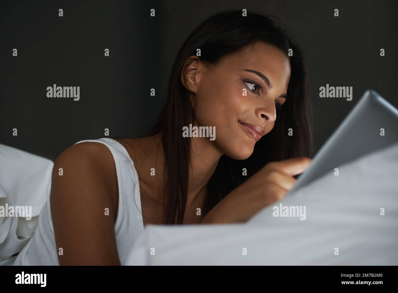 Nuit sur le net. une belle jeune femme se reposant au lit avec sa tablette. Banque D'Images