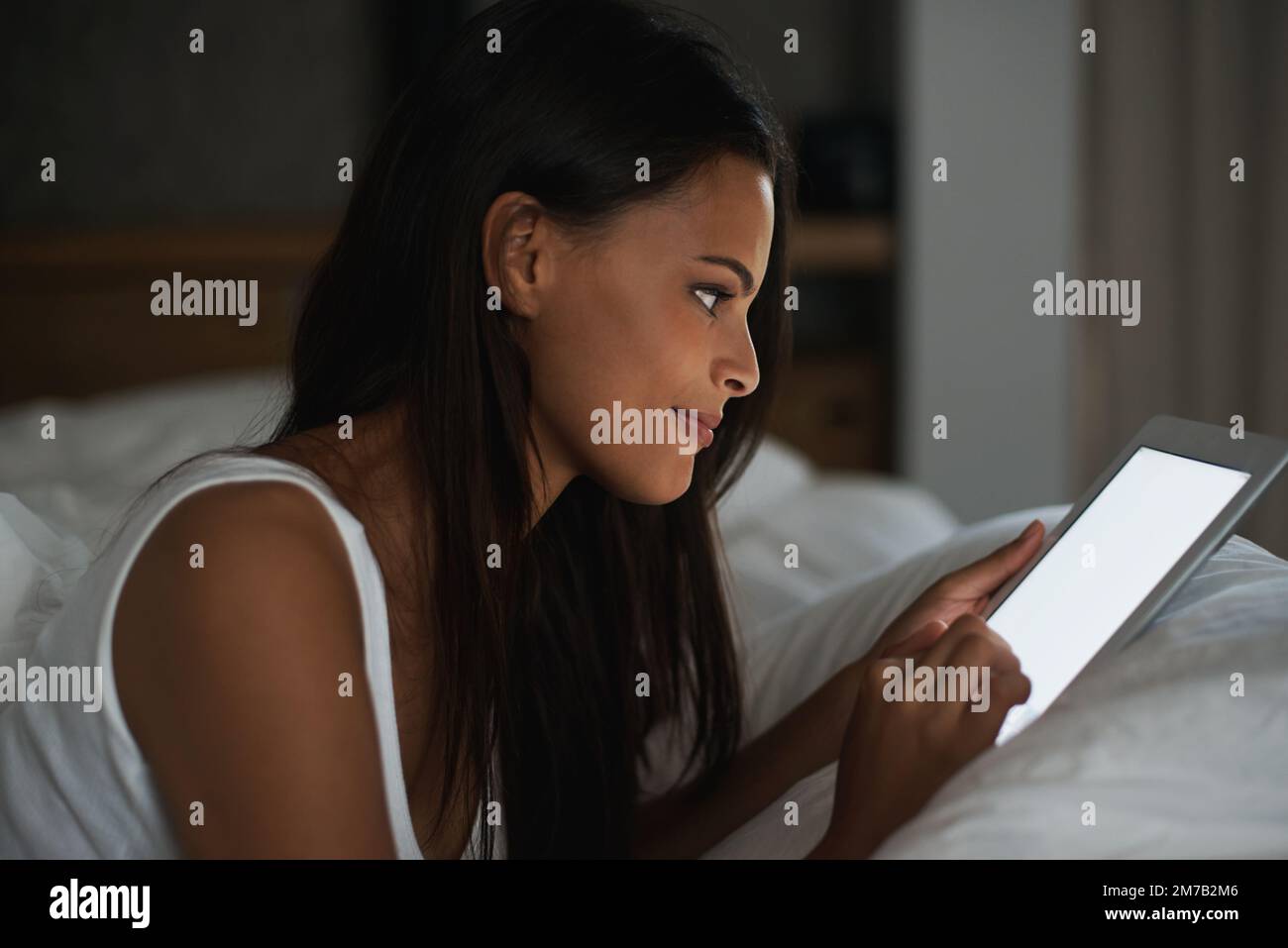 Brille dans l'obscurité. une belle jeune femme se reposant au lit avec sa tablette. Banque D'Images