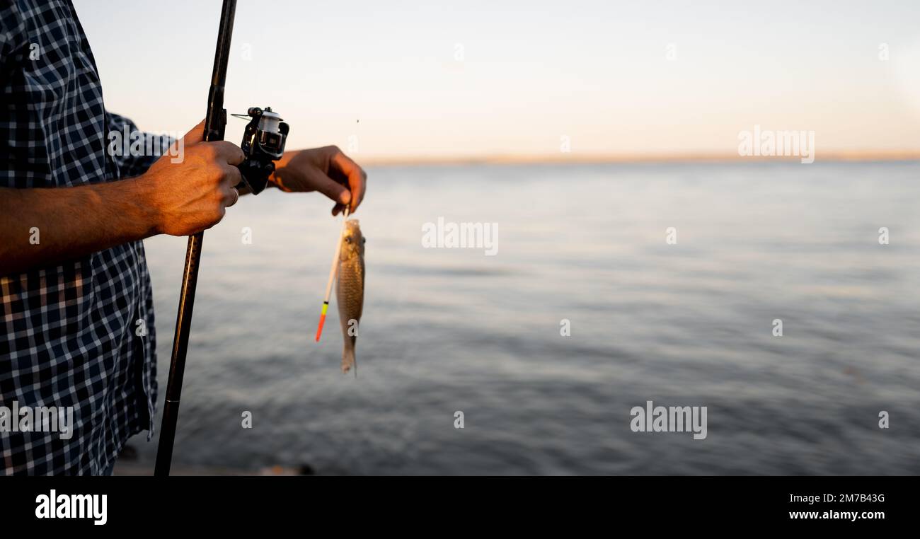 Poisson pêché accroché à la canne à pêche, lac en arrière-plan, à l'extérieur. passe-temps, activité, loisir, concept de pêche. Banque D'Images