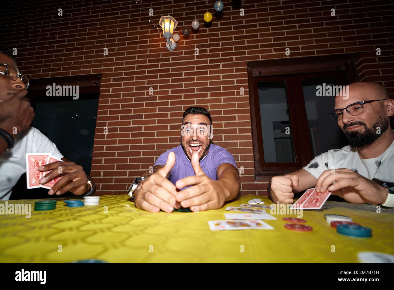 L'homme heureux et excité gagne dans le jeu de cartes de poker tout en jouant avec des amis. Banque D'Images